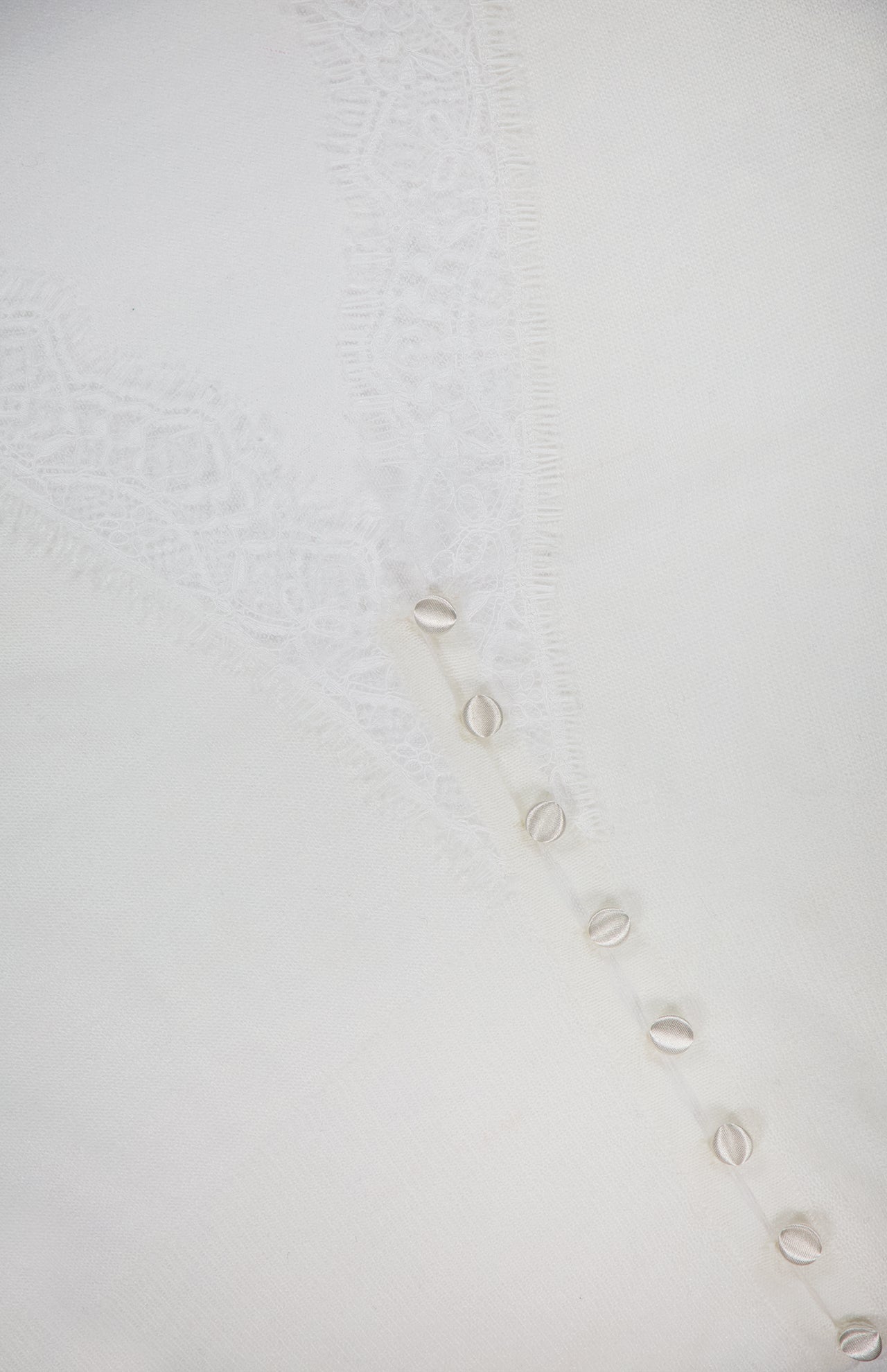 A close-up of the Eluna Lace Detail Cardigan by L'AGENCE, featuring an off-white hue with a lace pattern and a row of small cowrie shells for a delicate, elegant look.