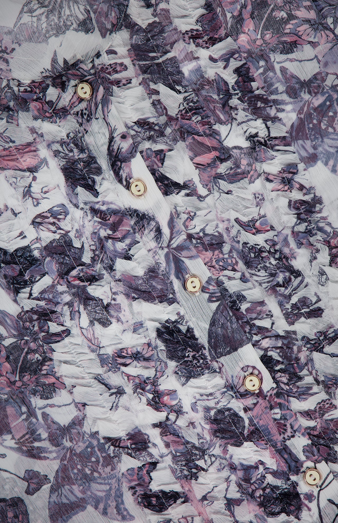 Close-up of the Eunice Ruffle Sleeve Blouse by L’AGENCE, featuring crinkled chiffon with a purple and white abstract floral print and vertical rows of beige buttons for a layered, dimensional look.