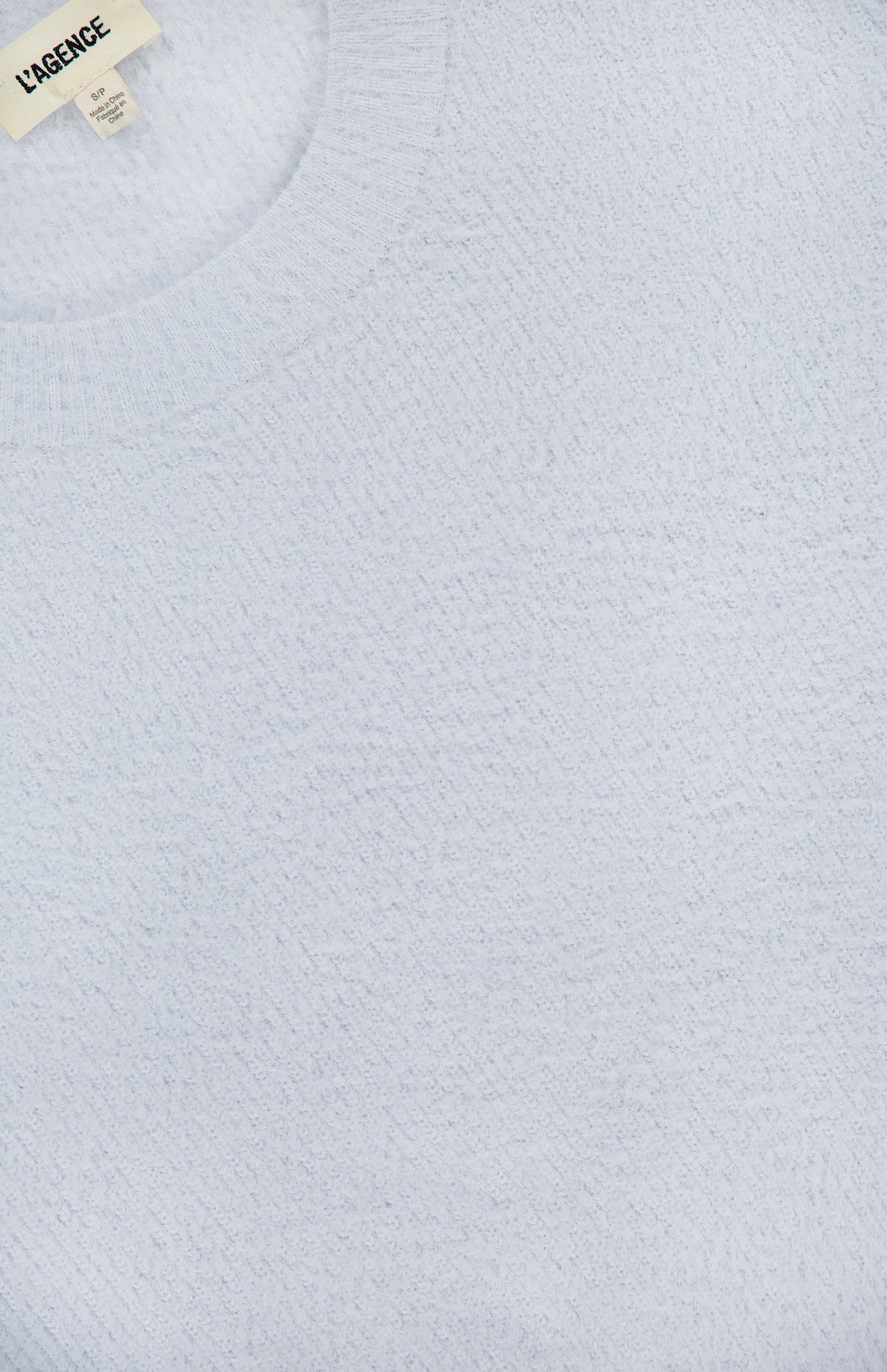 Close-up of a pale blue Guinevere Short Sleeve Cropped Crewneck Shirt by L'AGENCE, featuring textured knit and ribbed neckline. A small tag inside the collar reads L'AGENCE.