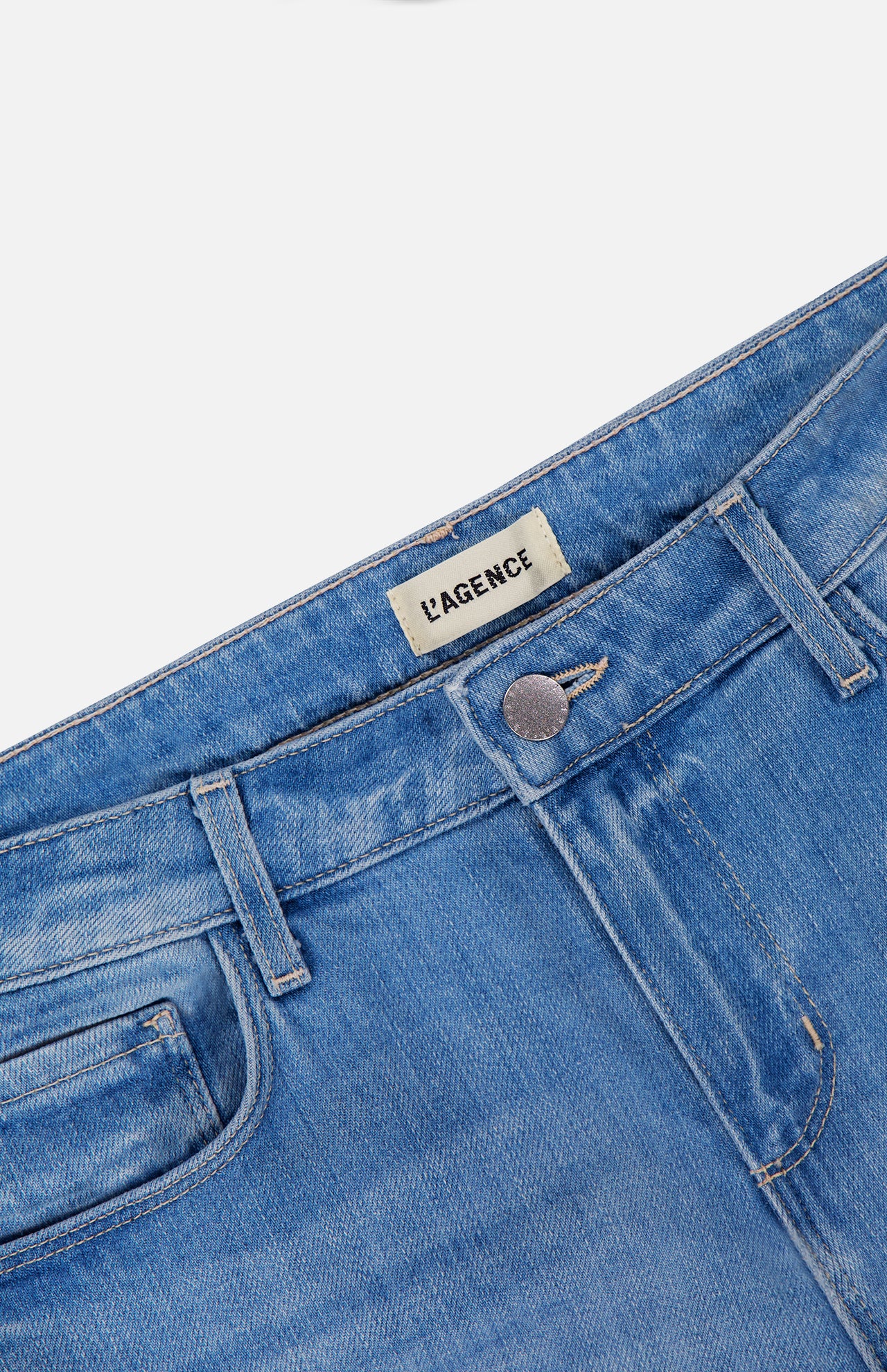 Close-up of the waistband and upper portion of L’AGENCE Joanne Low Rise Wide Leg Jean in Pacific, featuring light blue vintage denim, a metal button, and an interior L’AGENCE brand label.