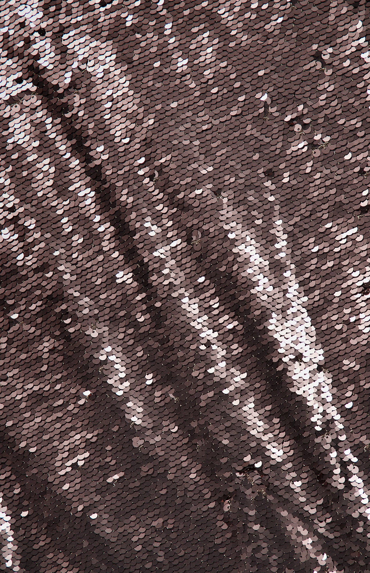 Close-up of the L’AGENCE Karma Sequin Maxi Dress, featuring fabric densely covered in small, shiny rose gold sequins reflecting light and forming a shimmering, textured surface with diagonal patterns—an elegant choice for special occasions.
