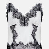 The Kimber Lace Insert Cami by L'AGENCE is a white satin cropped camisole featuring black lace trim at the neckline, hem, and seams, plus thin adjustable straps for a delicate, sophisticated look.