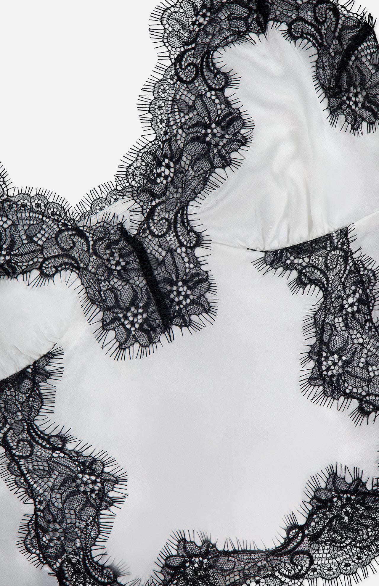 Close-up of the Kimber Lace Insert Cami by L'AGENCE, a white satin camisole with black floral lace trim, delicate eyelash edges, and adjustable straps for a perfect fit.