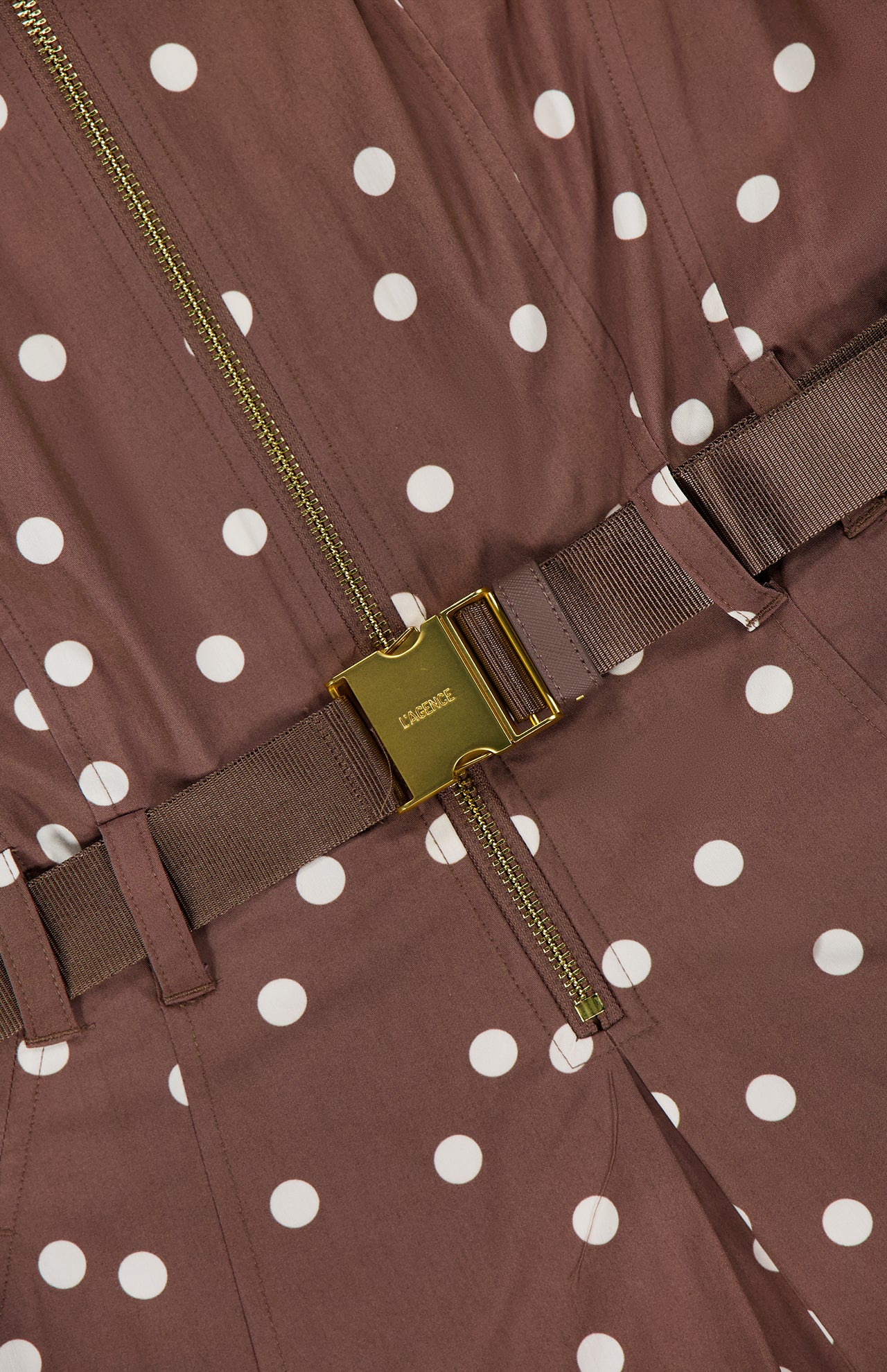 Close-up of the Kylo Belted Shirt Dress by L'AGENCE, featuring brown poplin fabric with white polka dots, a gold zipper, and a brown belt with a gold LANCEL buckle. The material is light and tailored in a classic shirt dress style.