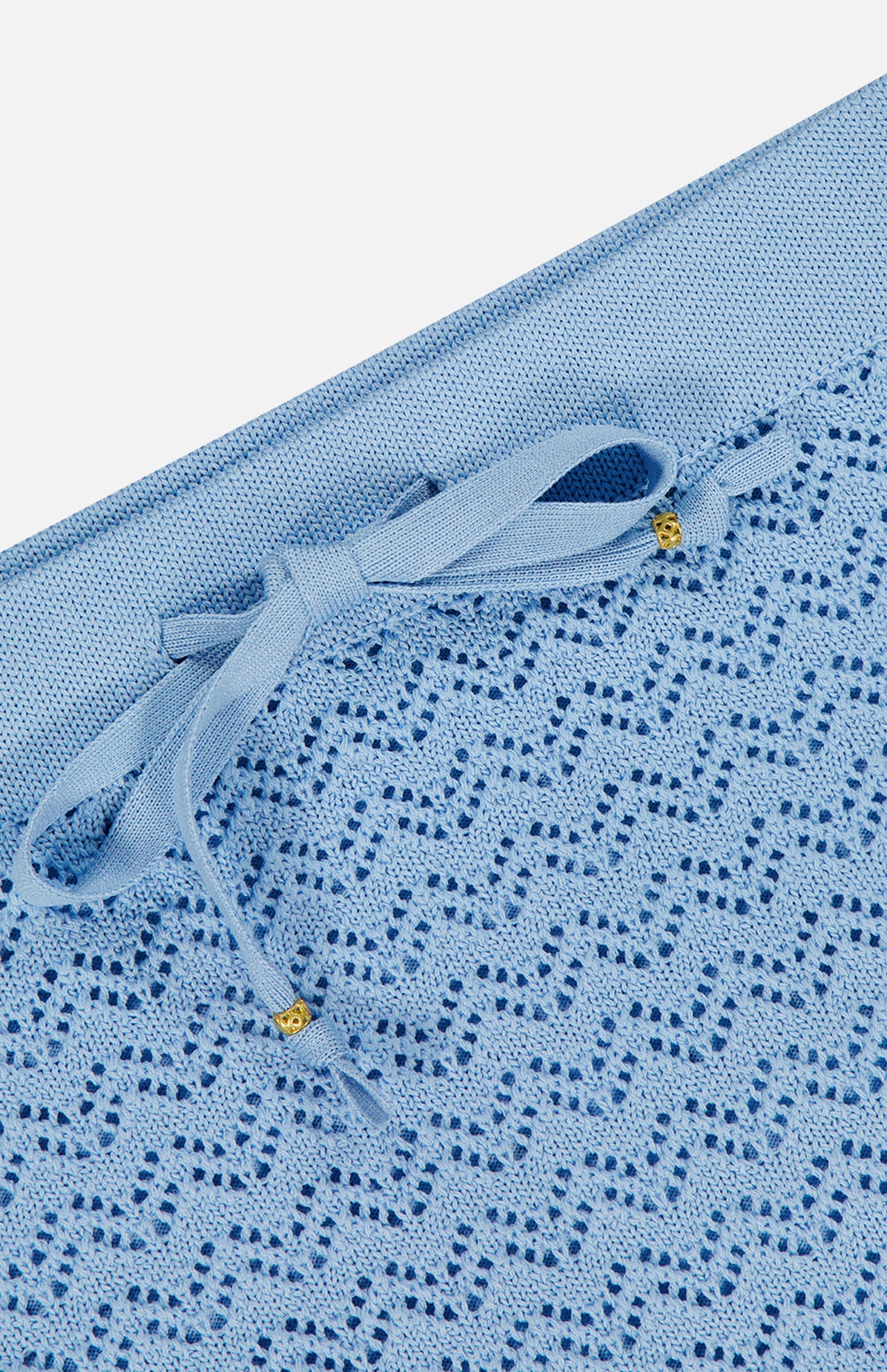 Close-up of the Lacen Pointelle Knit Skirt by L'AGENCE, crafted in powder blue soft knit with a decorative pattern and a drawstring waist finished with gold-tipped bows.