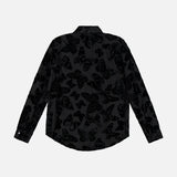 The Laurent Button Up Butterfly Blouse by L’AGENCE is a long-sleeve, black statement top featuring a subtle, semi-transparent butterfly pattern throughout. It is shown from the back against a plain white background.