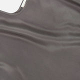 A close-up of the Lexi Silk Charmeuse Camisole by L’AGENCE, featuring soft gray silk, a scoop neckline, adjustable straps, and a visible inner tag.
