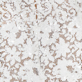 Close-up of the L'AGENCE Makena Sequin Pencil Skirt, featuring white lace with intricate floral patterns and sequins, a central seam, and delicate see-through texture against a beige background. Perfect for bridal parties or elegant occasions.