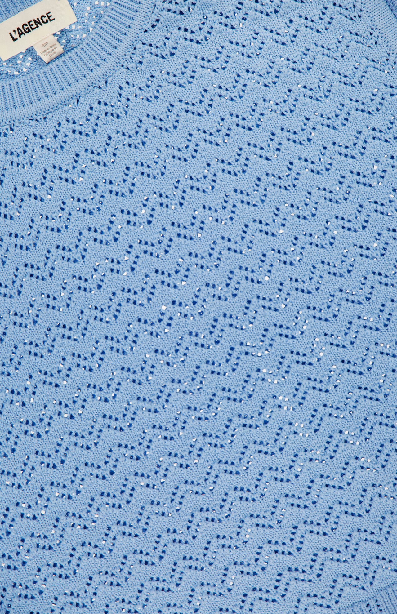 Close-up of the Max Pointelle Knit Top by L'AGENCE in powder blue, featuring a wavy, perforated pattern. A portion of the L'AGENCE label appears at the top left.