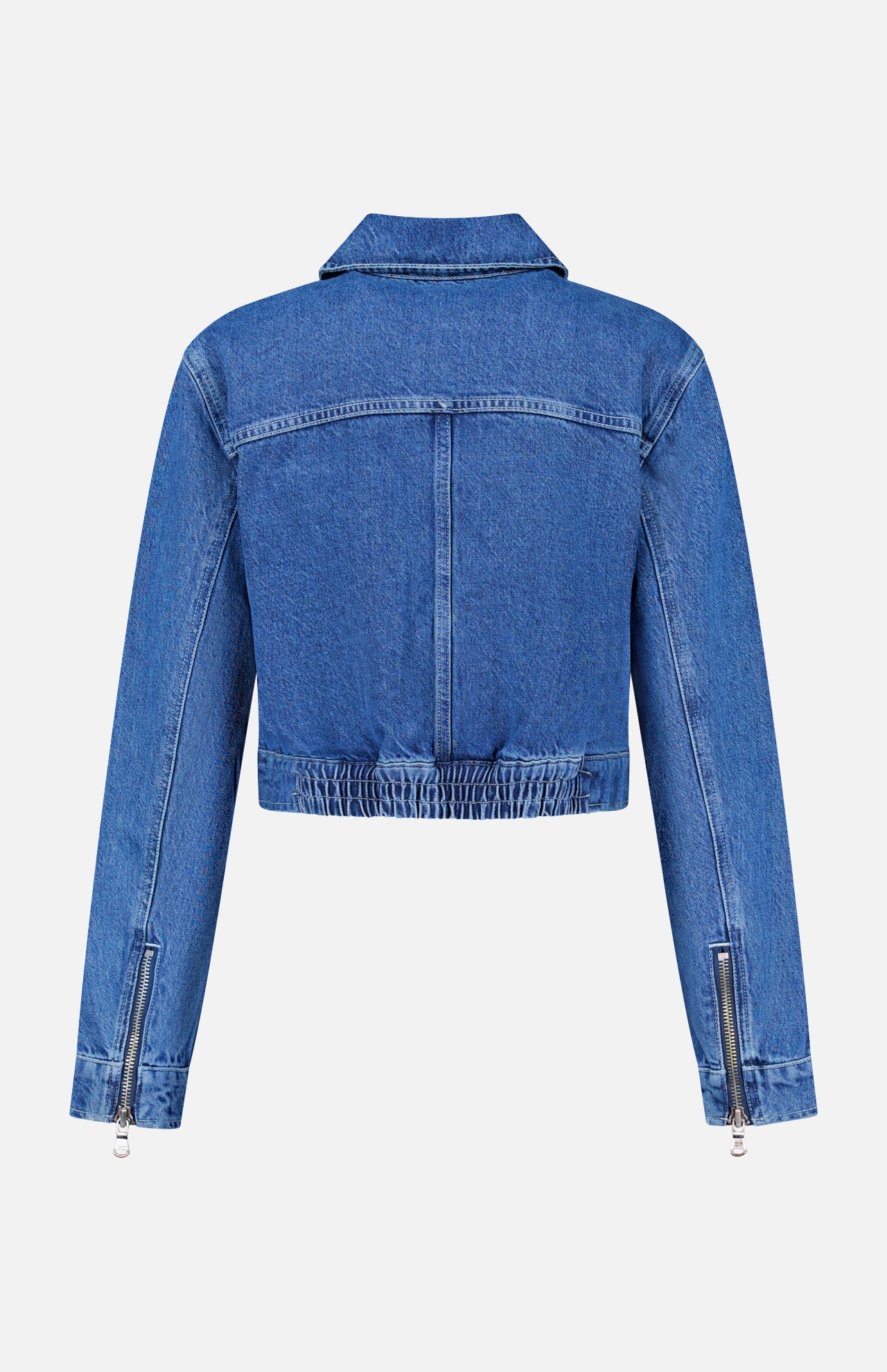 The Micah Oversized Denim Jacket by L’AGENCE is shown from the back in blue denim, featuring long sleeves with zipper details and an elasticized waistband. This jacket boasts visible seam stitching, an oversized fit, and a classic collar for a timeless look.