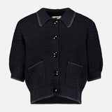 The Novalie Waffle Stitch Short Sleeve Cardigan by L’AGENCE features a short-sleeved, black textured knit design with a collar, large black buttons down the front, and two front pockets—offering effortless feminine style to any outfit.