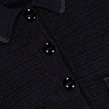 Close-up of the L’AGENCE Novalie Waffle Stitch Short Sleeve Cardigan, showcasing its textured black fabric, four shiny black buttons, and visible pocket—evoking the refined elegance of a classic cardigan. The label near the collar reads L’AGENCE.