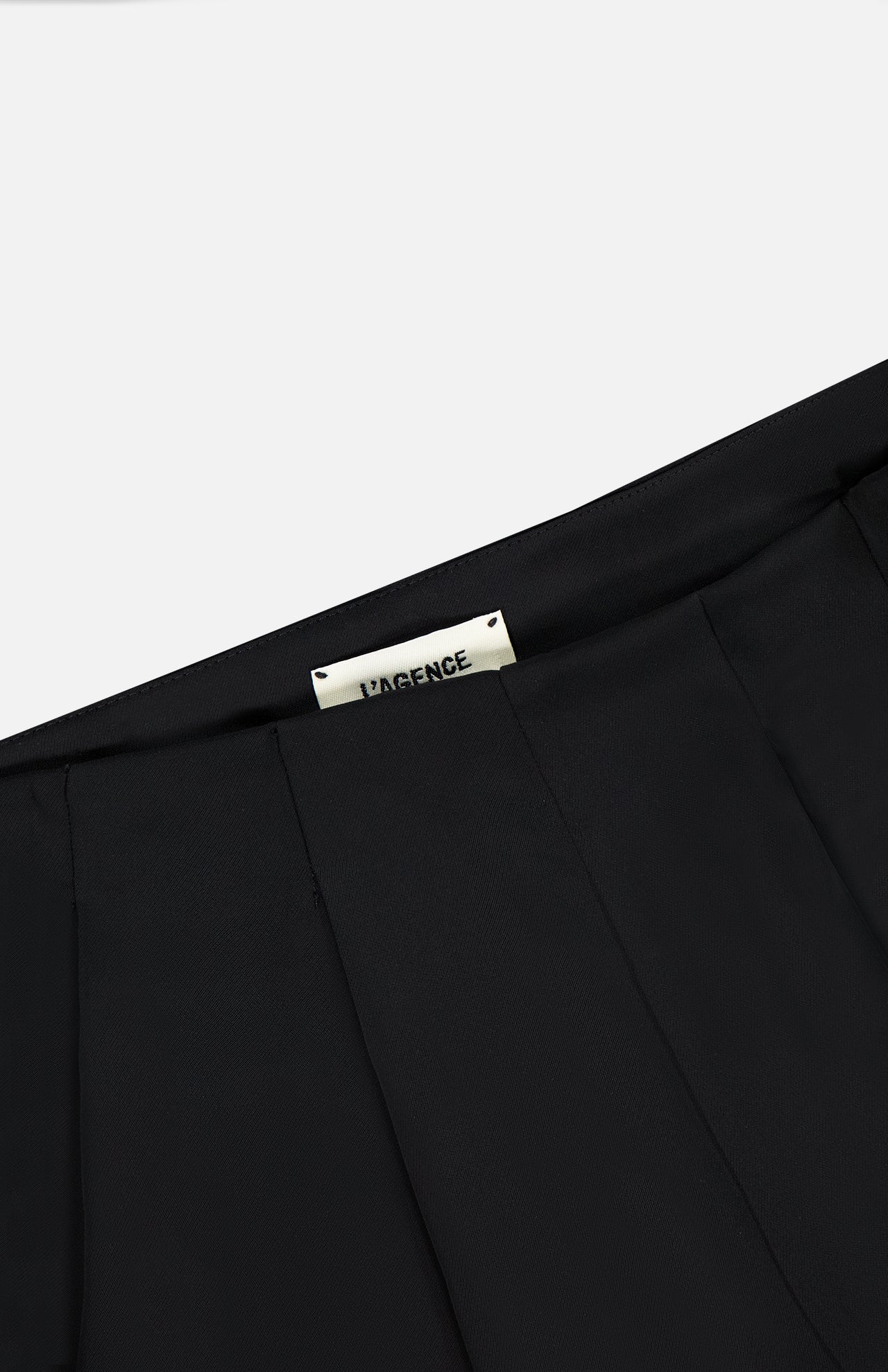 Close-up of the waistband on the black Novalynn Cropped Pleated Pant, featuring pleats and a white inner label with L'AGENCE branding in black.