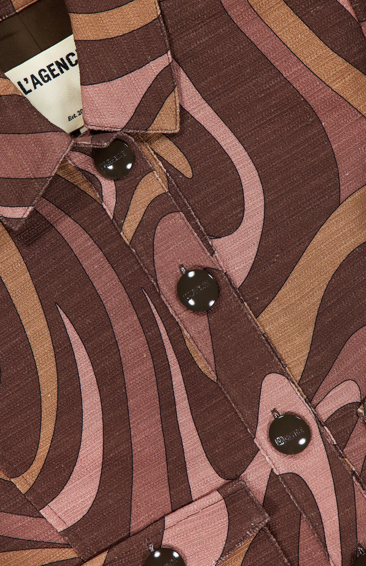 Close-up of the Nyx Cropped Swirl Print Jacket by L'AGENCE, showcasing sepia tones with swirling pink patterns, black buttons, and a visible label on the inside collar.