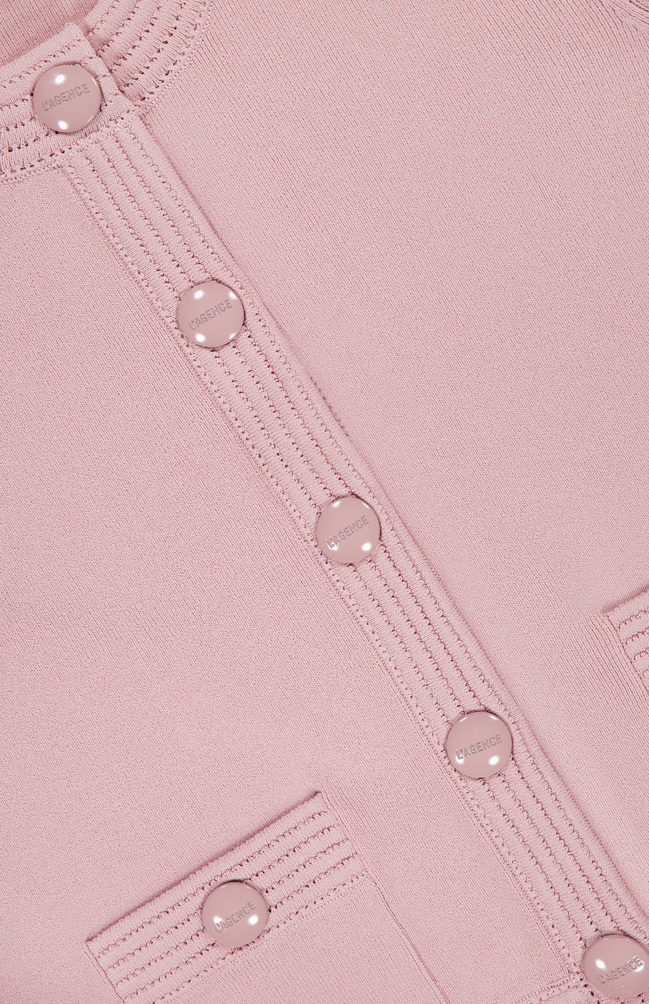 Close-up of the Patsy Crop Crewneck Cardigan by L'AGENCE in blush, featuring round shiny buttons engraved with the brand name, ribbed detailing along the button placket, and the tops of two small front pockets.