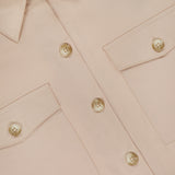 Close-up of the Pearson Military Pocket Blouse by L'AGENCE in light pink poplin, featuring two front chest pockets and beige buttons. The partially visible L'AGENCE label adds a chic touch to this versatile button-down top.