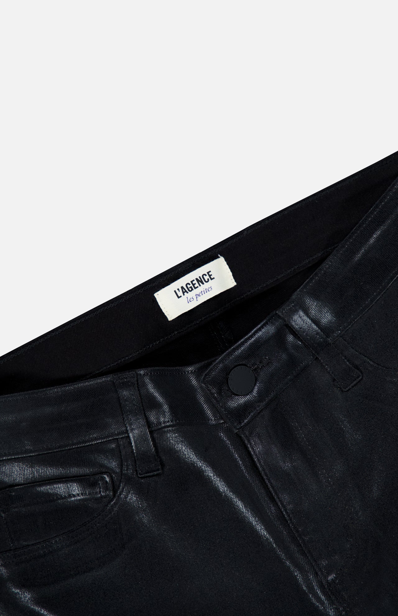 Close-up of the waistband and upper portion of the Petite Kendra High Rise Crop Flare in Noir by L’AGENCE, featuring shiny black coated denim with belt loops, pockets, a button closure, and a white L’AGENCE label. The background is plain and light-colored.