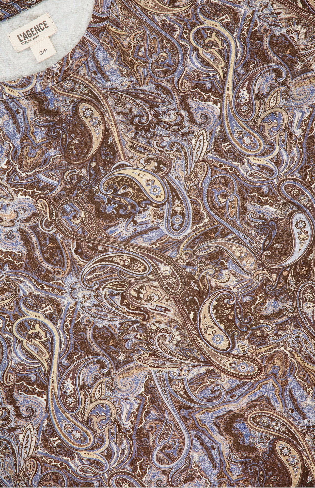 Close-up of the Ressi Short Sleeve Ditsy Paisley Shirt by L’AGENCE, featuring brown, beige, and blue paisley fabric with swirling floral motifs. The L'AGENCE label is visible at the top left corner.