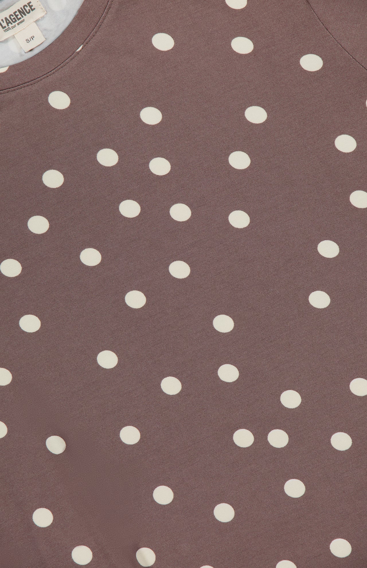 Close-up of the Ressi Short Sleeve Crewneck Polka Dot T-shirt by L'AGENCE, featuring a mauve color with white polka dots. The stretch jersey fabric label appears partially at the top left corner.
