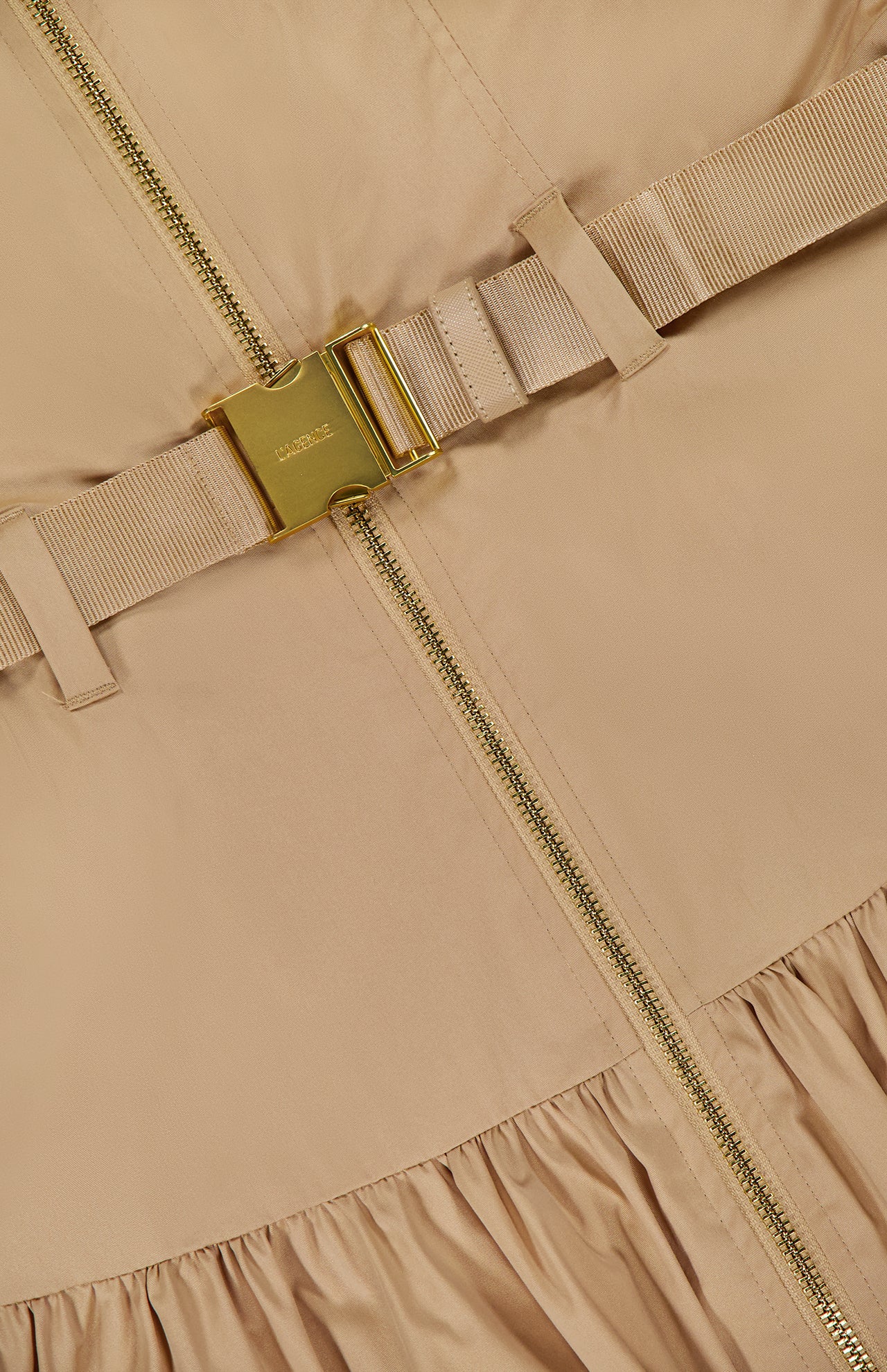 Close-up of the L'AGENCE Rima Belted Maxi Dress in light brown, showcasing a gold zipper, matching beige fabric belt with gold buckle, and gathered hem detail.