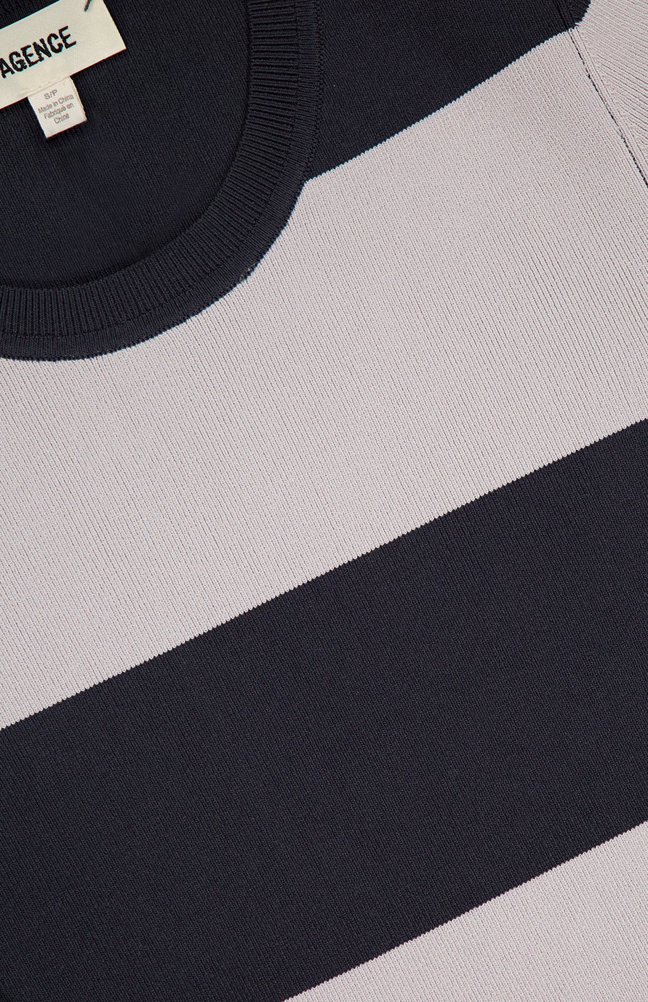 Close-up of the L'AGENCE Rosemond Crewneck Short Sleeve Bodysuit, featuring wide black and light gray stripes, textured knit fabric, a ribbed collar, contouring fit, and a partial clothing label at the upper left corner.
