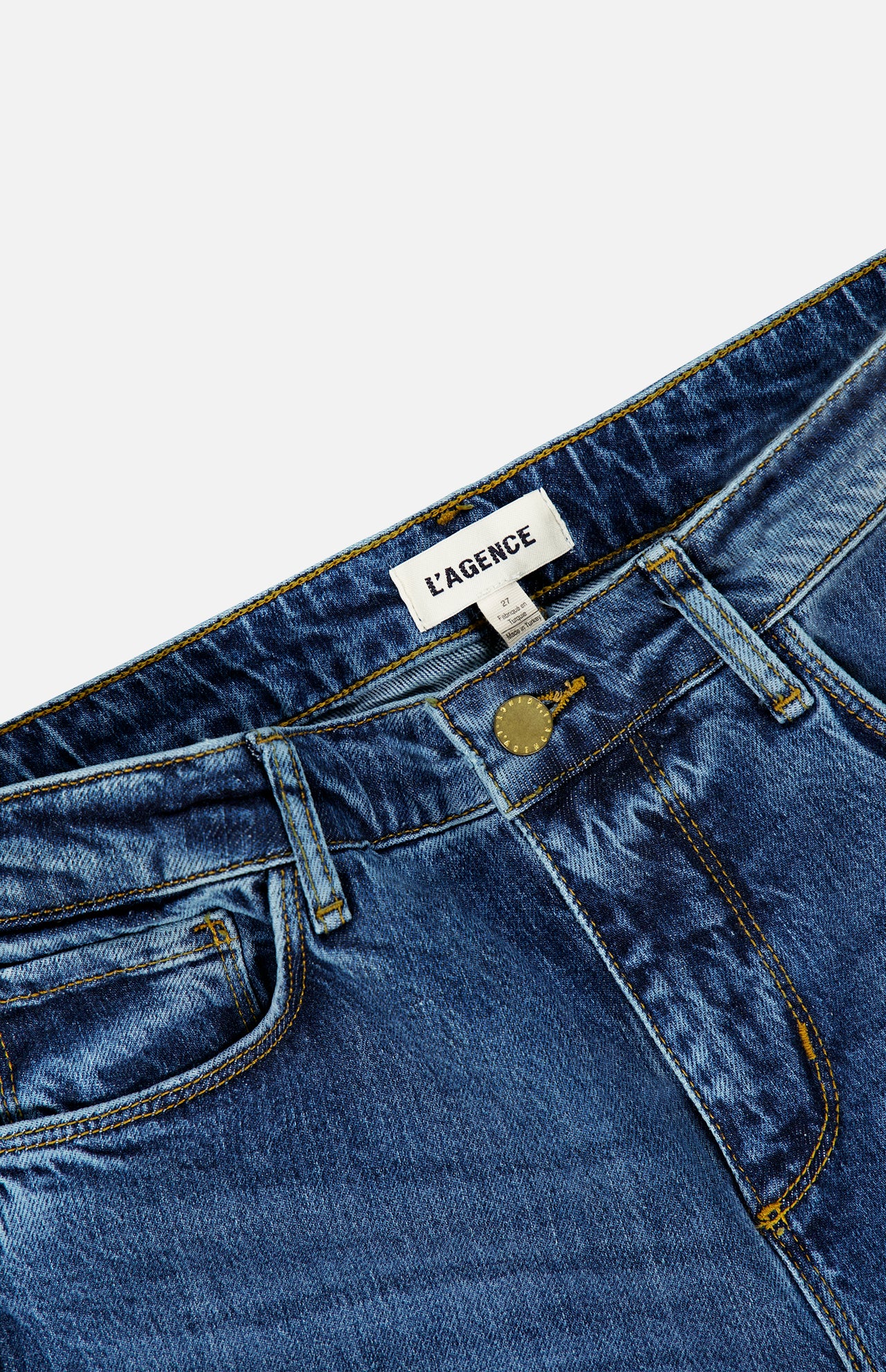 Close-up of the Ruth High Rise Straight Jean in Newcastle by L’AGENCE, crafted from premium stretch denim in blue. These jeans feature yellow stitching, a metal button, belt loops, and a white label with “L’AGENCE” on the inside waistband. The high-rise design and straight leg silhouette offer timeless style and comfort.