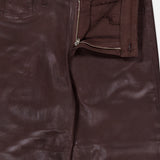 Close-up of the Ruth High Rise Straight Pant by L’AGENCE, crafted from maroon coated denim in a slim straight-leg silhouette with a high rise, partially open zipper fly, visible button, and pocket. The L’AGENCE label is sewn inside the waistband.