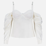 The L'AGENCE Saya Cold Shoulder Draped Top features an off-white hue, long puffed sleeves, thin adjustable straps, and a fitted bodice—an elegant choice for evening. Shown against a plain white background.