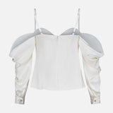 The Saya Cold Shoulder Draped Top by L'AGENCE is an off-white satin blouse featuring dramatic puffed sleeves, thin adjustable straps, a back zipper, subtle sheen, and fitted cuffs with small buttons—perfect for evening wear.