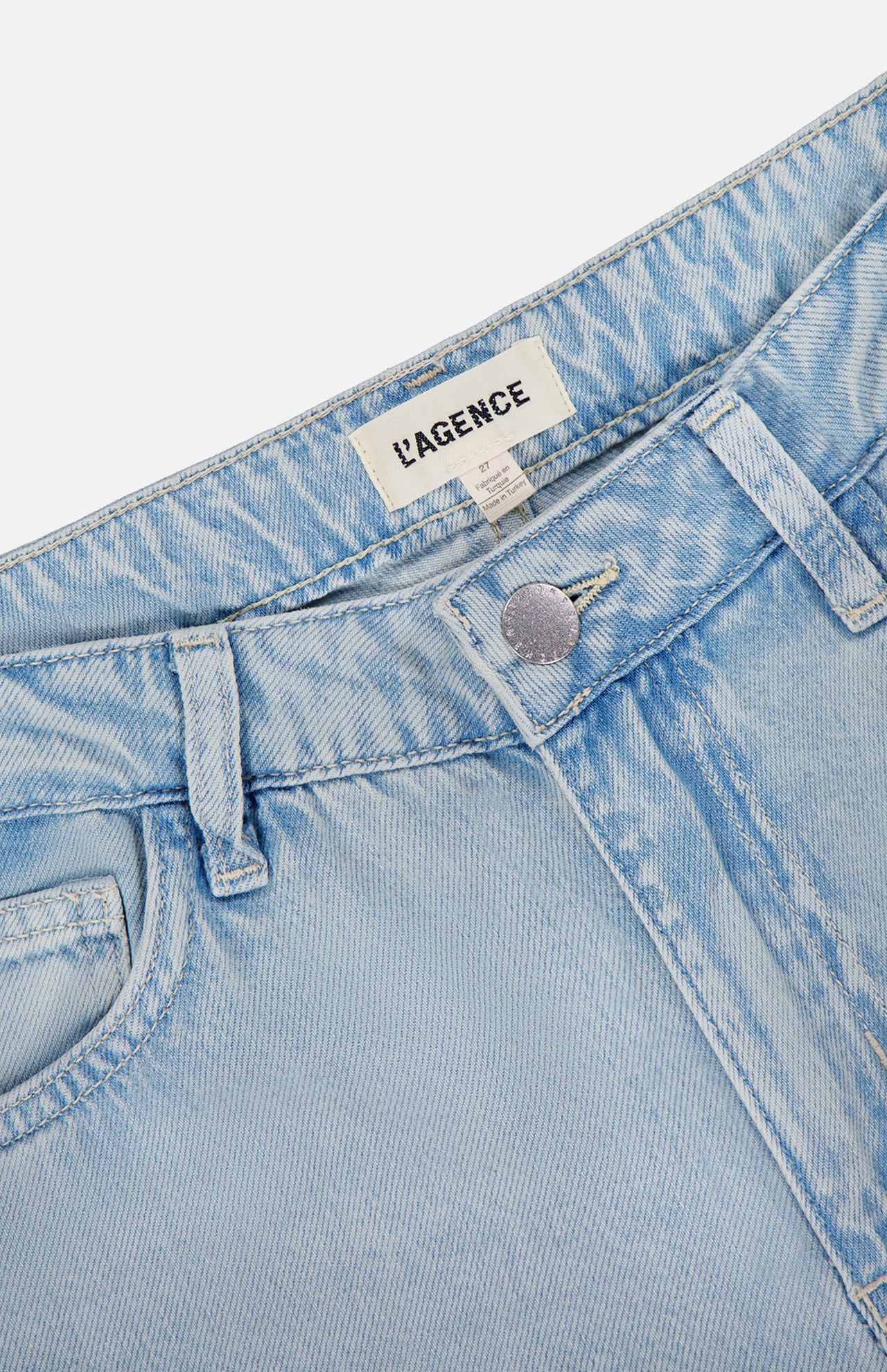 Close-up of the waistband and top button of the Scottie High Rise Wide Leg Jean in Lago by L’AGENCE, featuring light blue denim, visible brand label inside, belt loops, and part of the front pocket.