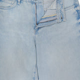 The Scottie High Rise Wide Leg Jean in Lago by L'AGENCE features light blue denim with a partially open zipper and button fly, shown lying flat on a white surface. The waistband label displays the L'AGENCE brand name.