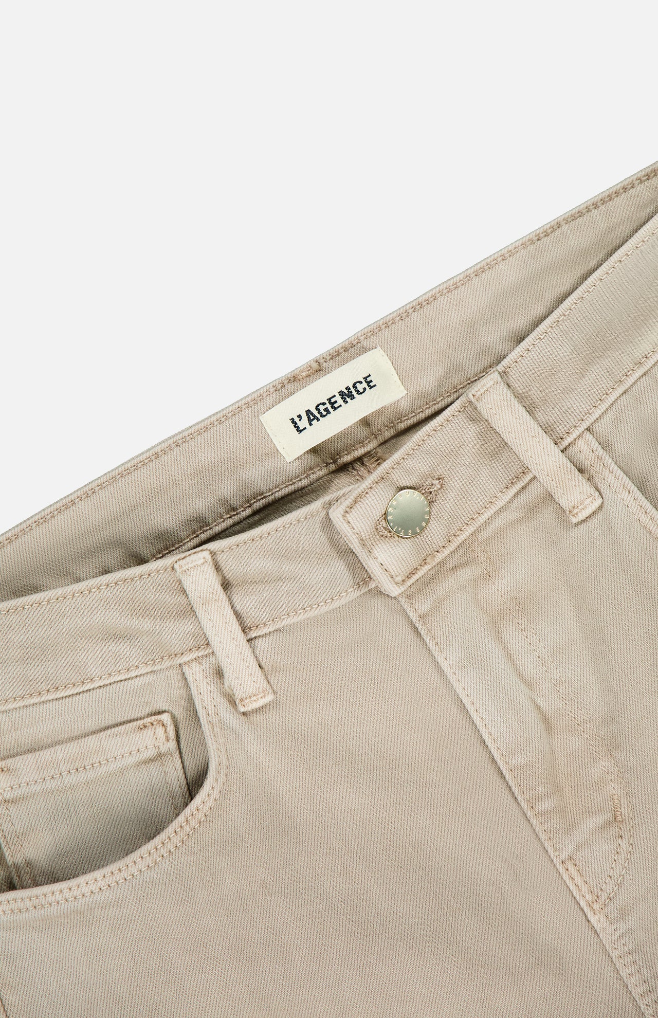 Close-up of the waistband and front pocket on the Selma High Rise Sleek Baby Boot Pant in Biscuit by L'AGENCE, showing a metallic button and visible inner waistband brand label.