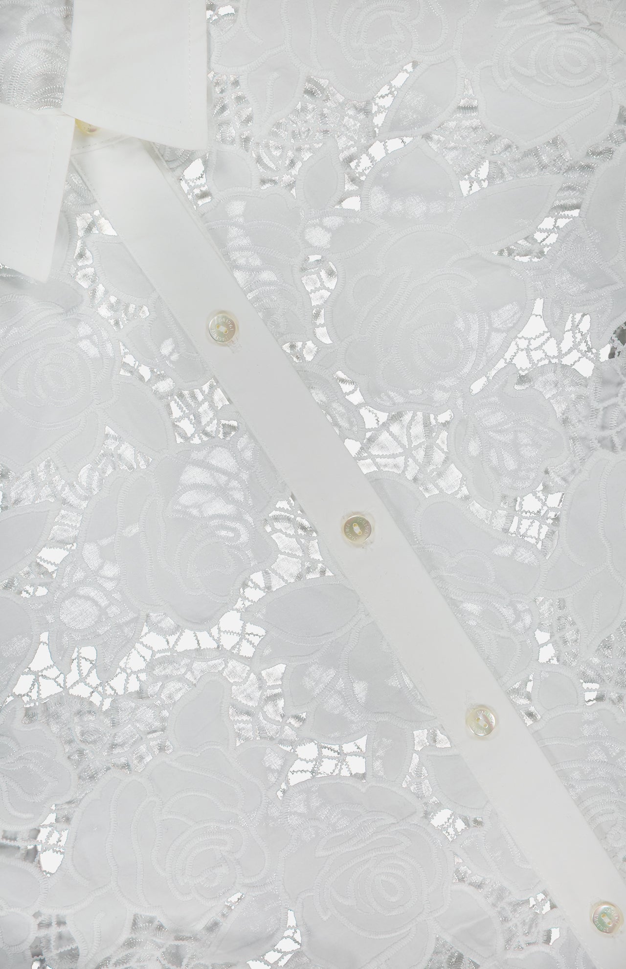 Close-up of the Seychelle Cropped Button Down Shirt by L'AGENCE, featuring white eyelet fabric with intricate floral lace, a white buttoned placket, pointed collar, pearl-like buttons, and elegant rose designs.