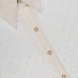 Close-up of the L'AGENCE Sophie Long Sleeve Blouse featuring a sheer Swiss dot fabric, beige collar, polka dot pattern, and beige buttons down the front. The fabric label is partially visible at the top left.