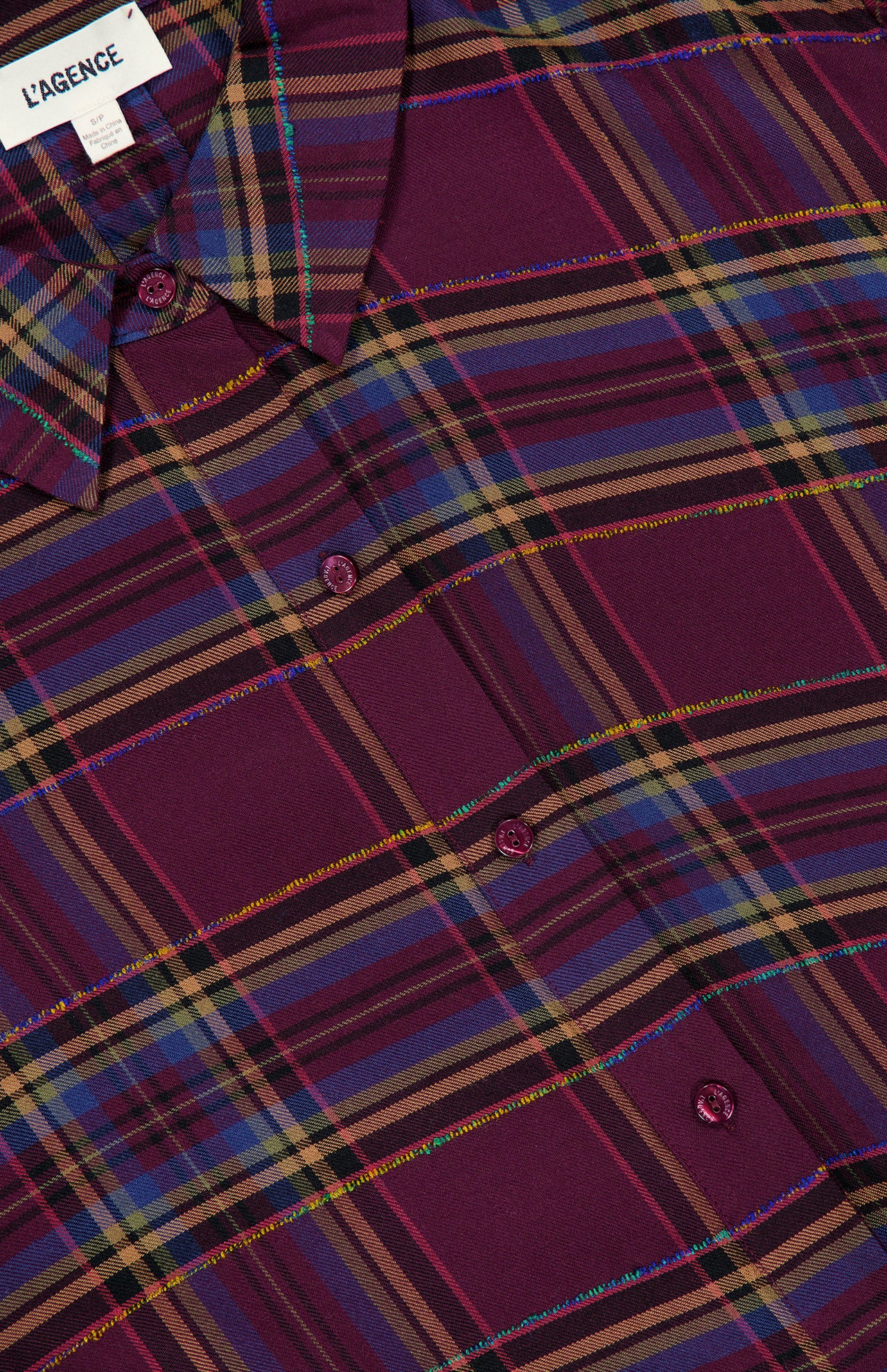 Close-up of the L’Agence Suzette Hi Low Shirt in a purple, blue, and yellow plaid pattern with metallic thread accents, a high-low hem, and a back slit detail.