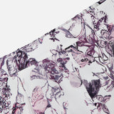 Close-up of the Sylie Butterfly Print Pull On Short by L'AGENCE, showcasing white fabric with pink and purple florals, butterfly motifs, a pleated seam detail, partial waistband, and a comfy pull-on fit.