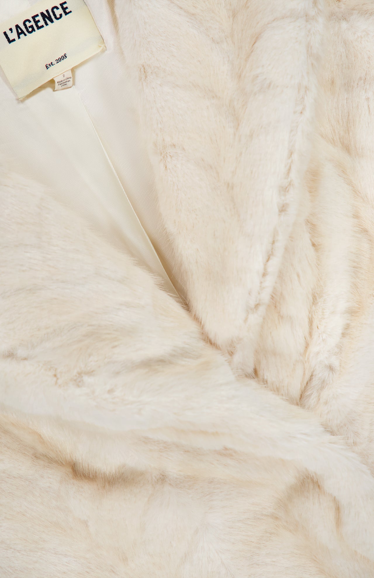 Close-up of a champagne Toira Faux Fur Coat by L’Agence, featuring a large lapel and a visible brand label at the collar.