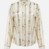 The Tyler Long Sleeve Belt Print Blouse by L’AGENCE is a women’s satin button-up adorned with a sophisticated beige and gold belt and buckle pattern over an elegant ecru background. Perfect for any occasion, this blouse effortlessly adds refined style to your wardrobe.
