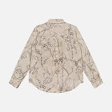 The Tyler Long Sleeve Chain Print Blouse by L'AGENCE is a cream silk top with subtle horsebit motifs, tailored silhouette, curved hem, and buttoned cuffs, shown here from the back.