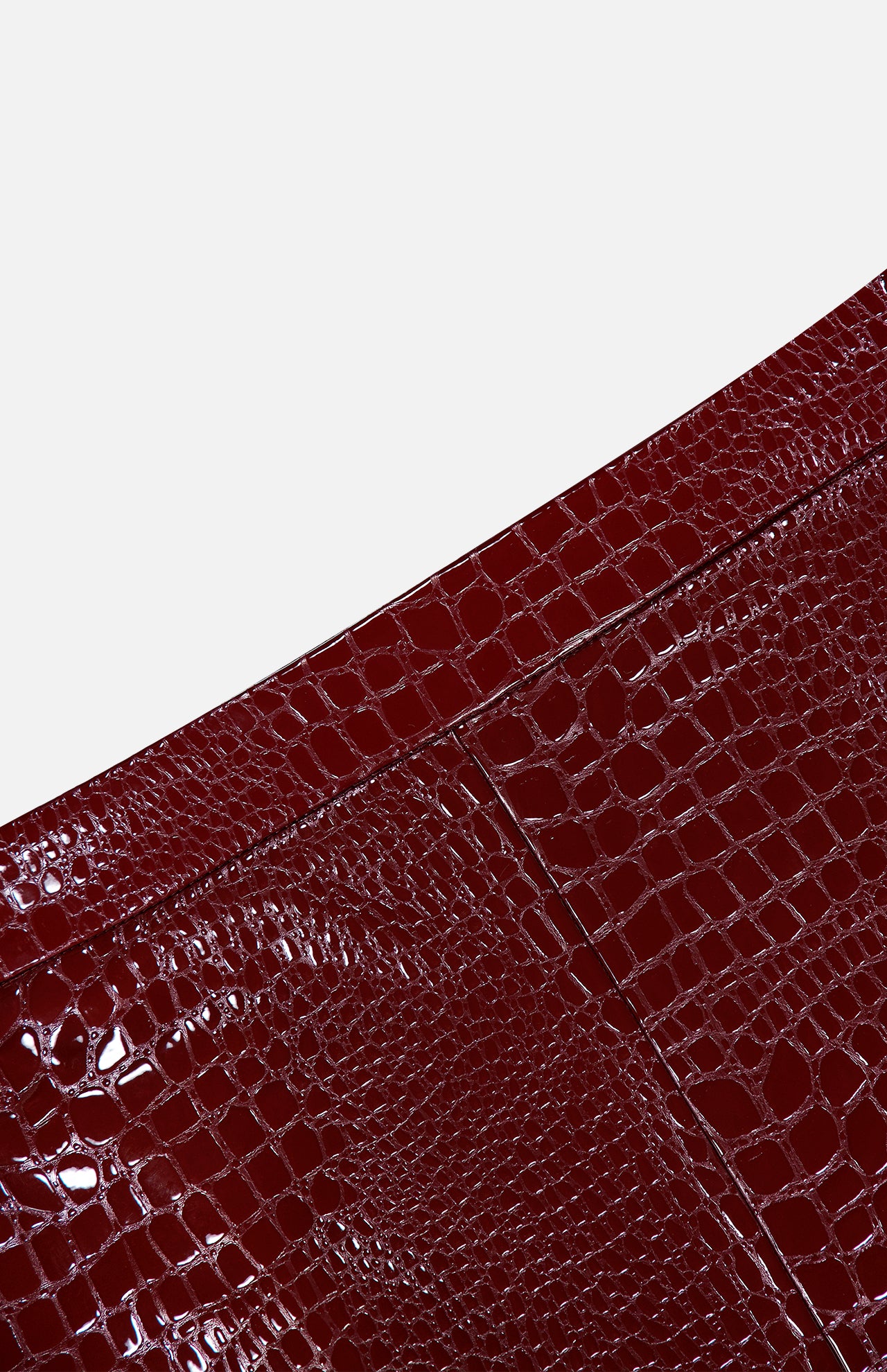 Close-up of the Violetta Pencil Skirt by L’AGENCE, featuring a glossy, dark red croc-embossed vegan leather with a patchwork design, set against a plain white background.