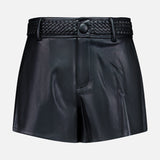 The Virelle Braided Waistband Short by L’AGENCE is crafted from black vegan leather, featuring a high waist, front button closure, and distinctive braided waistband detailing at the top. Western-inspired yet modern in design, these shorts are presented against a clean white background.