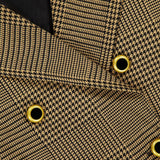 Close-up of the L'AGENCE Xoey Cropped Plaid Trench Coat, featuring brown and black houndstooth-patterned fabric with gold and black grommet details, overlapping layers reminiscent of a classic cropped trench silhouette, and a glimpse of the black inner lining.