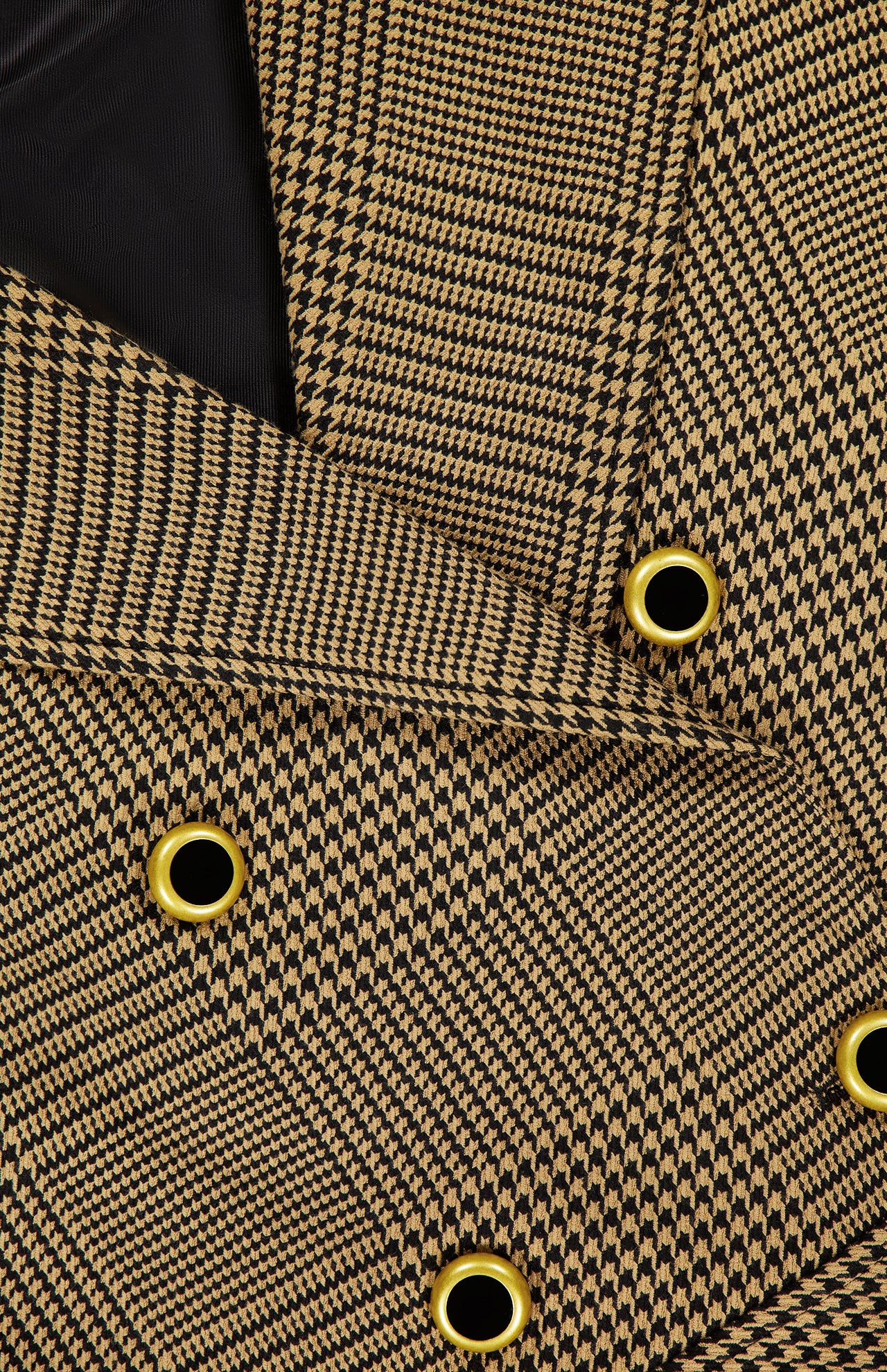 Close-up of the L'AGENCE Xoey Cropped Plaid Trench Coat, featuring brown and black houndstooth-patterned fabric with gold and black grommet details, overlapping layers reminiscent of a classic cropped trench silhouette, and a glimpse of the black inner lining.