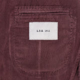 A close-up of the pocket on the Corduroy Single Breasted Sportcoat by L.B.M. showcases its rich maroon corduroy texture and a distinctive white label featuring “L.B.M. 1911” in black lettering, emphasizing the brand’s refined craftsmanship in this classic men’s jacket.