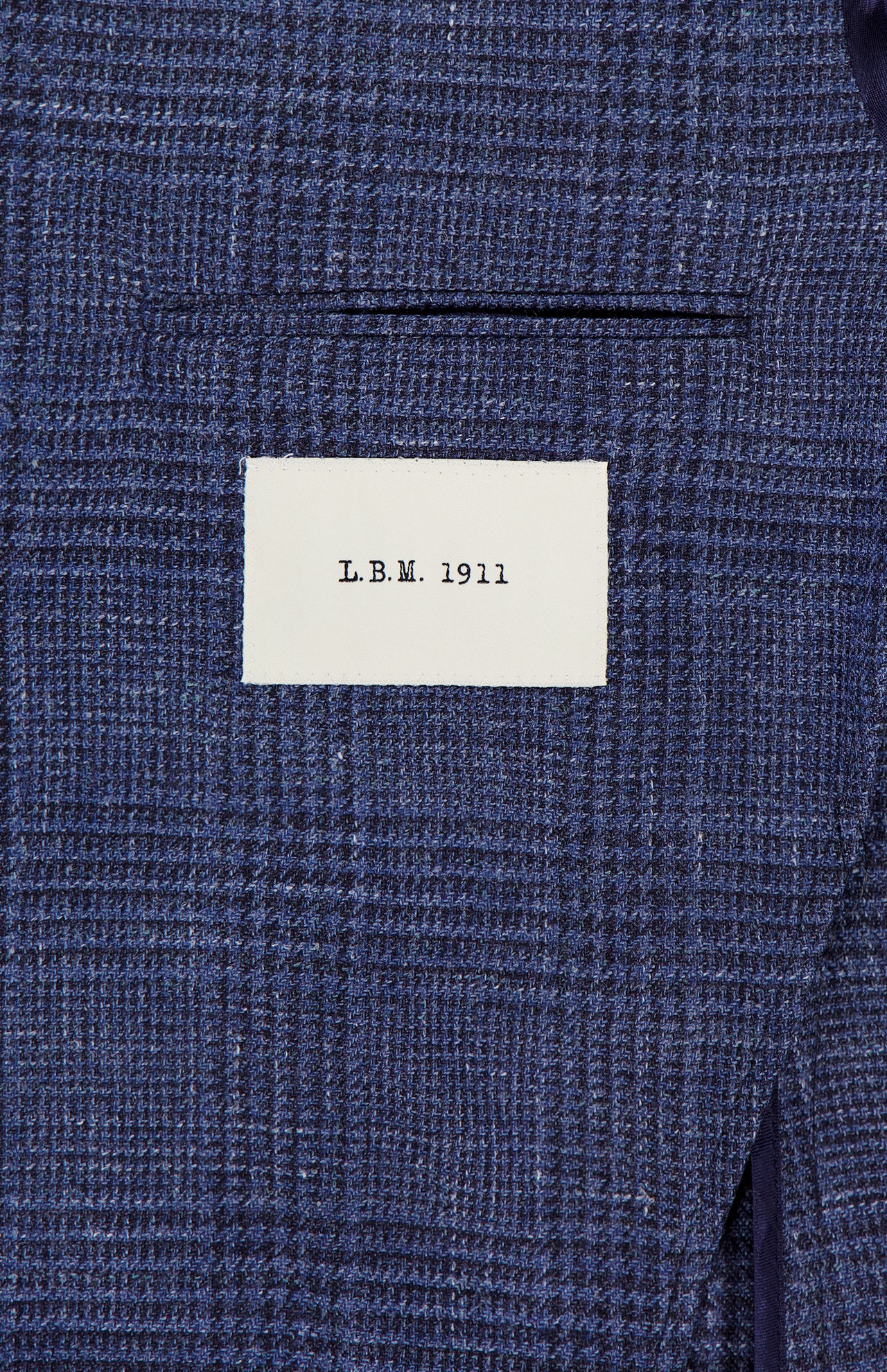 A close-up of the L.B.M. Glen Plaid 2 Button Sportcoat in blue, highlighting its refined wool-silk-linen blend fabric and tailored details, with a small white L.B.M. label above the pocket.