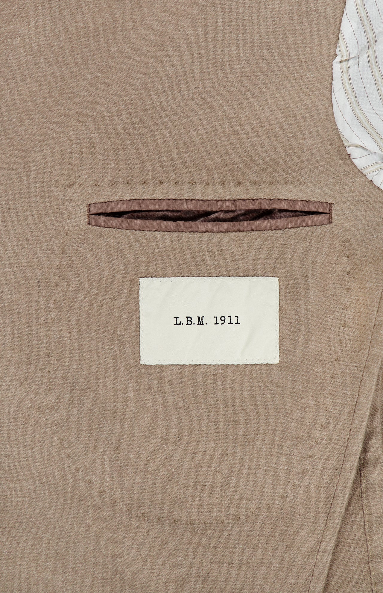 Close-up of the interior pocket of the Solid 2 Button Sportcoat by L.B.M., featuring a white label that reads L.B.M. 1911. A portion of striped fabric lining appears in the upper right corner, showcasing the refined craftsmanship of this wool cashmere blazer, expertly made in Italy.