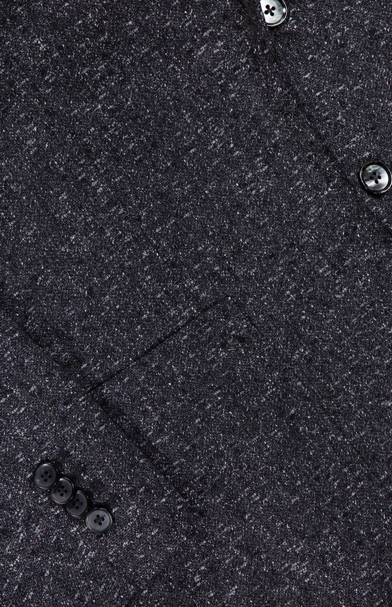 Close-up of the textured dark grey fabric of the L.B.M. Speck 2 Button Sportcoat, highlighting a front pocket, four black sleeve buttons, and two black front buttons arranged diagonally across the image. This modern sportcoat showcases expert L.B.M. craftsmanship for ultimate sophistication and style.