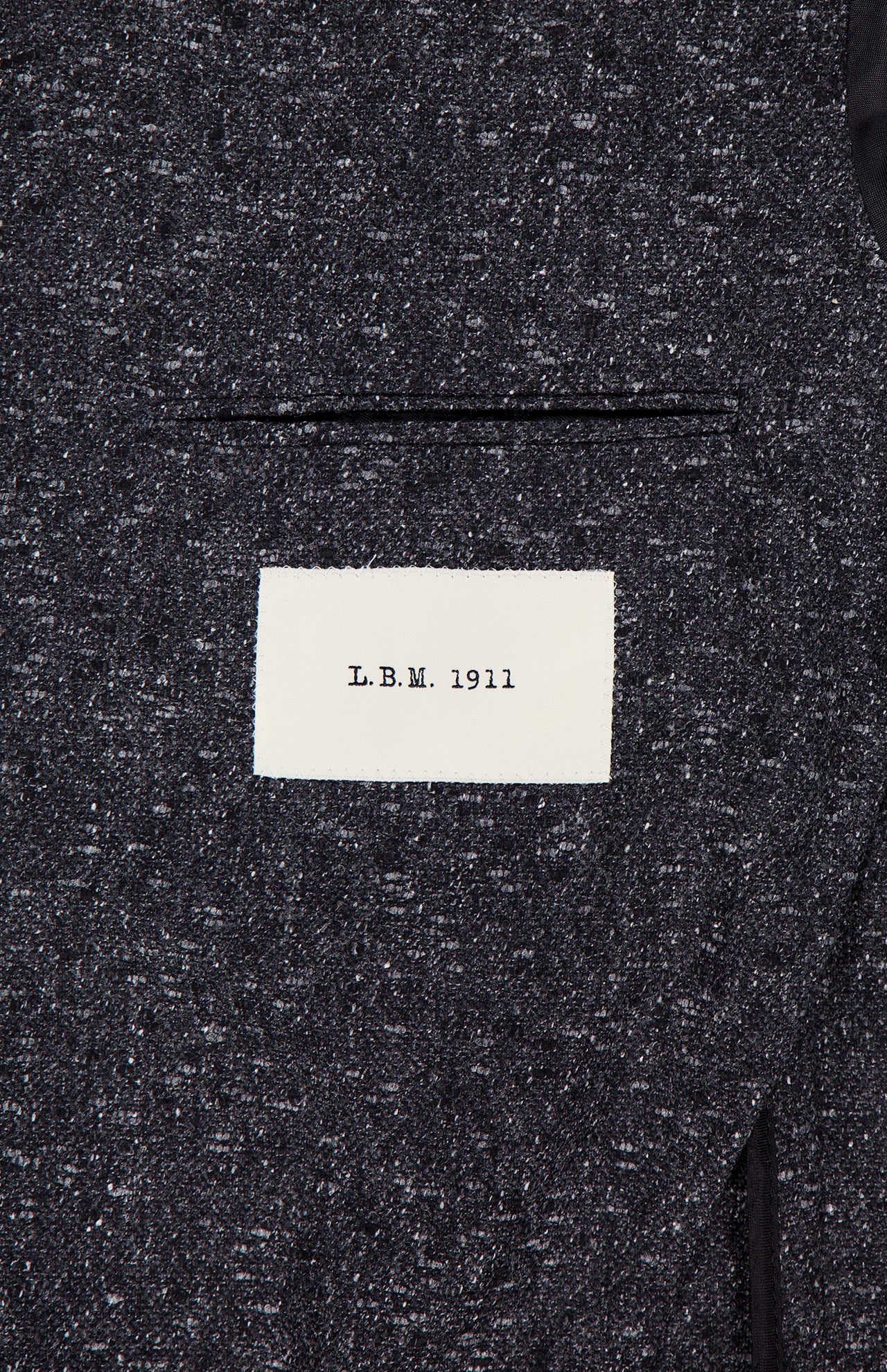 A close-up of the textured dark grey Speck 2 Button Sportcoat by L.B.M., made in Italy, featuring a white sewn-on label with "L.B.M. 1911" in black text.