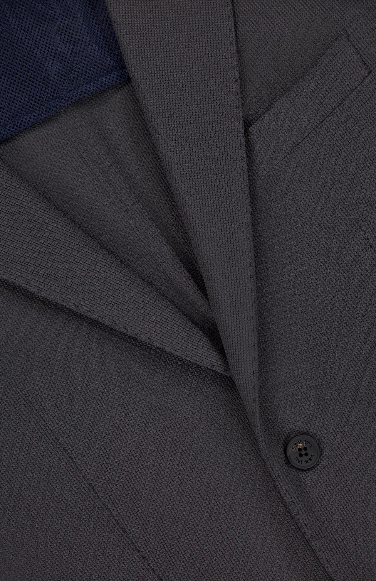 Close-up of the L.B.M. Travel Uniform Water-repellent Sportcoat in dark gray, highlighting its textured fabric, lapel, front pocket, single button, and a glimpse of the dark blue shirt or lining underneath.
