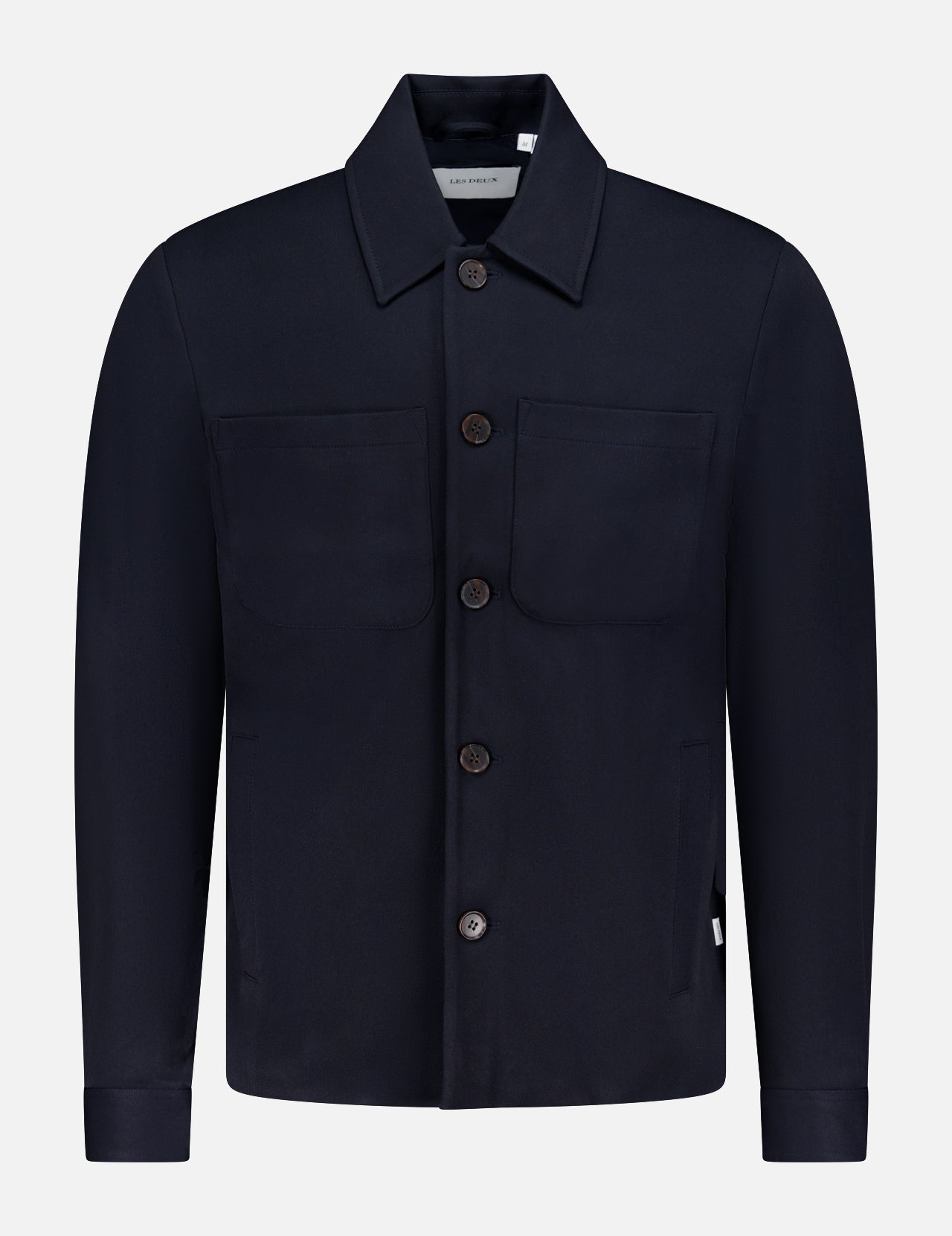 The LES DEUX Marseille Hybrid Shirt Jacket is a minimalist black button-up with a collar, two chest pockets, long sleeves, and a straight hem—ideal for modern menswear fans. Shown on a plain white background.